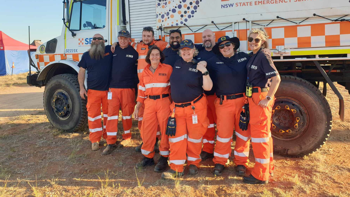 Group of diverse SES members standing in front of a SES truck wrapped with artwork