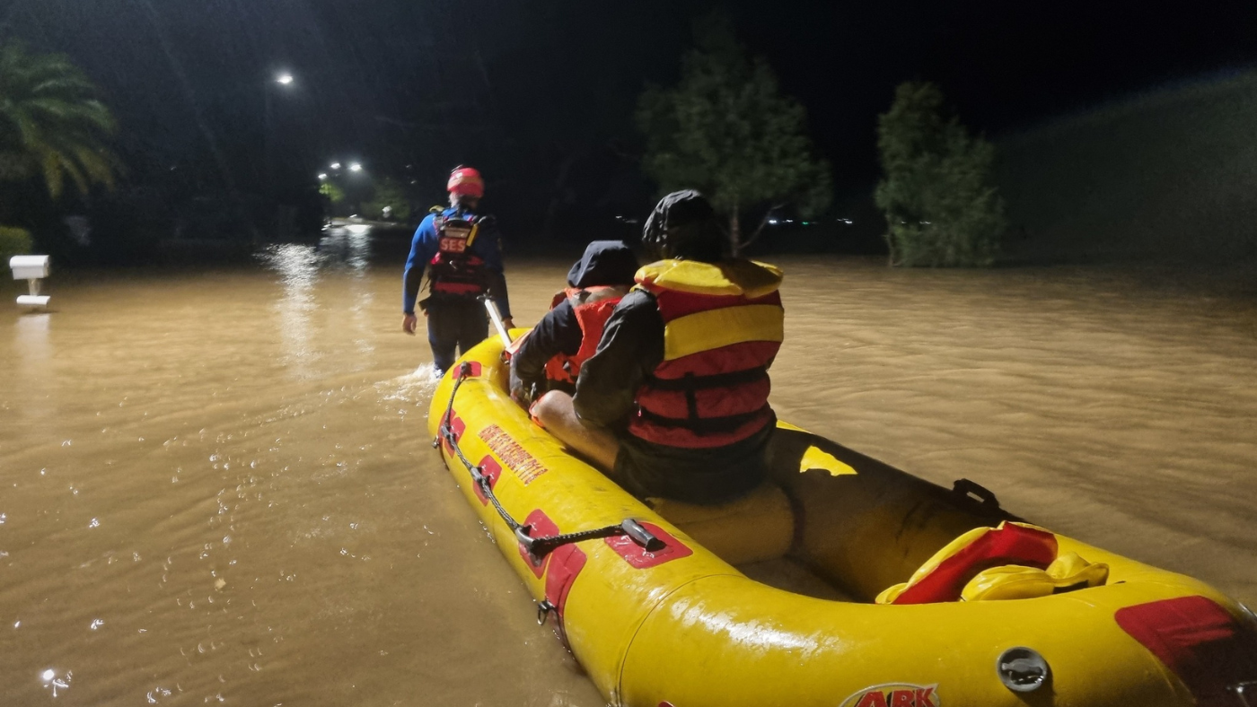A flood rescue operate pulls a flood boat through flood water with two passengers.