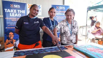 Three Lightning Ridge SES volunteers stand together, smiling as they cut into a large cake