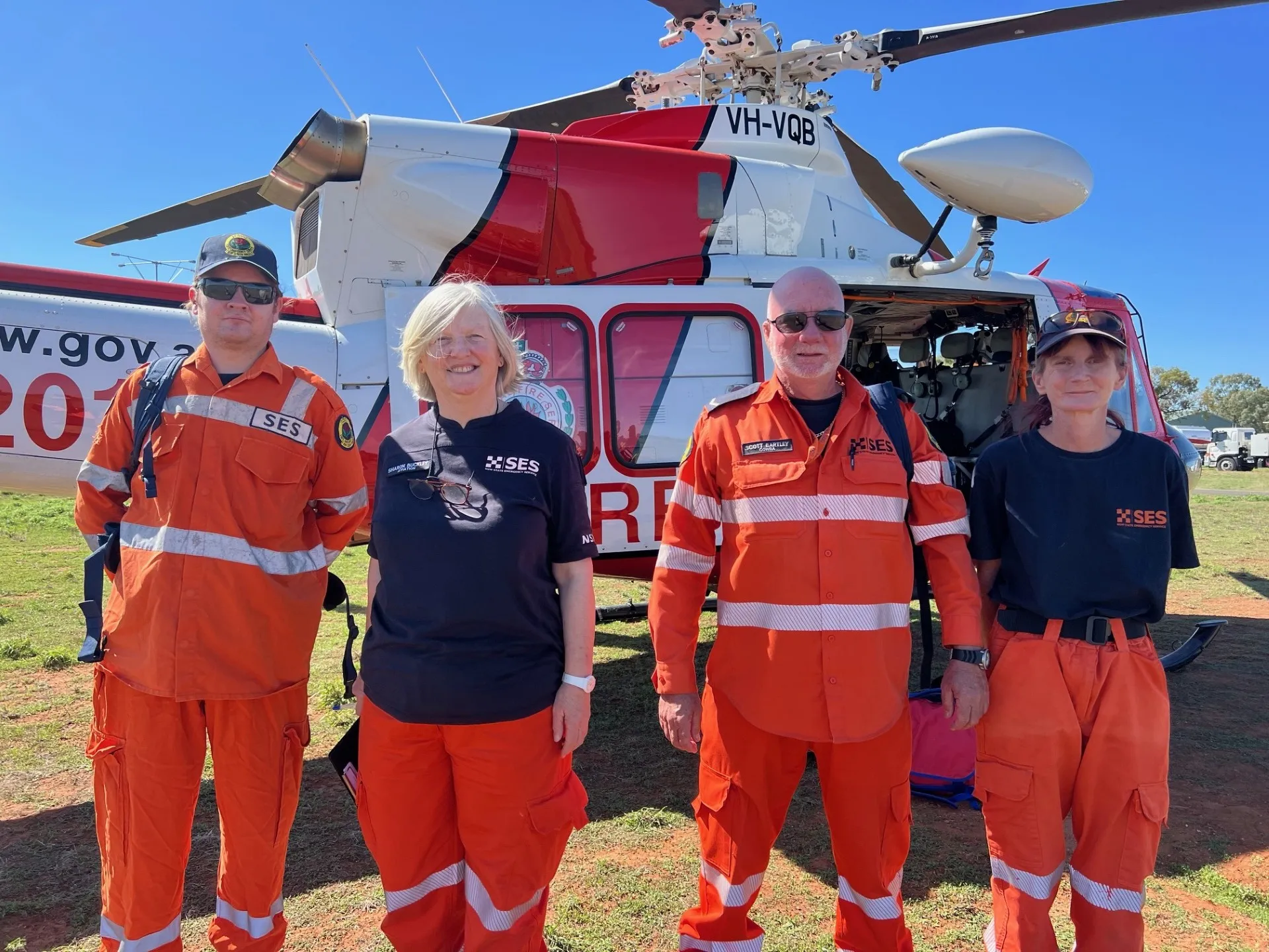 4 volunteers standing in front of a red and white helicopter