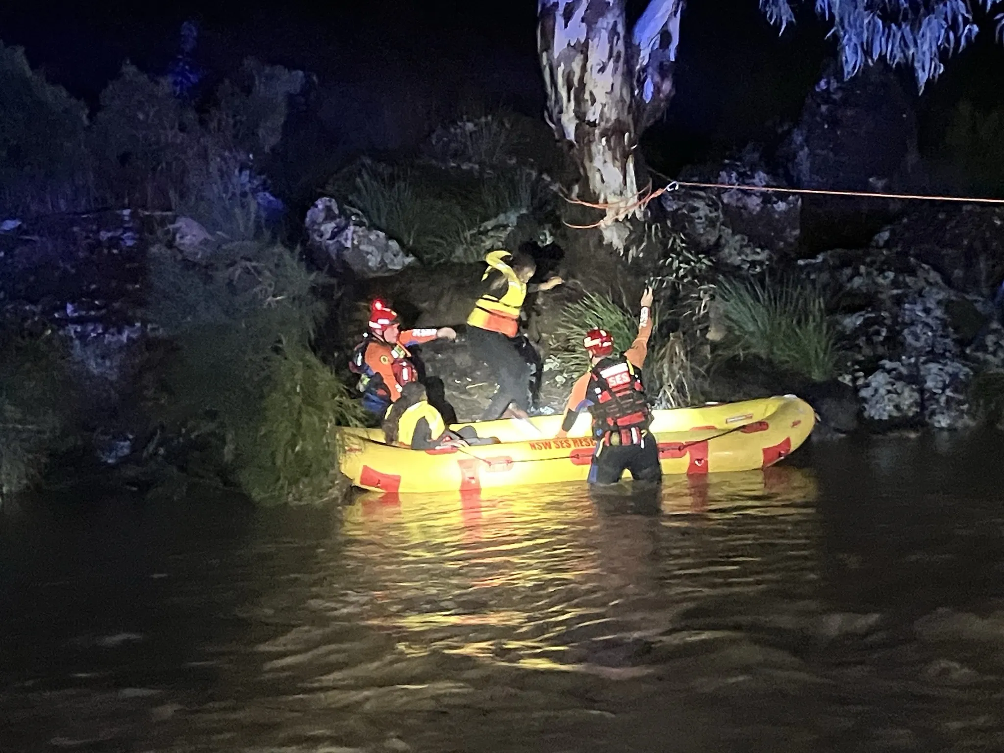 A woman is rescued by two flood rescue operators in a yellow boat on the side of a river.