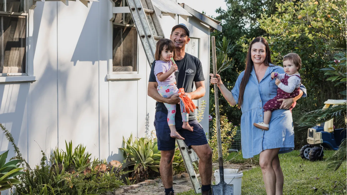 A family of four in front of a home holding a shovel with a ladder behind them.