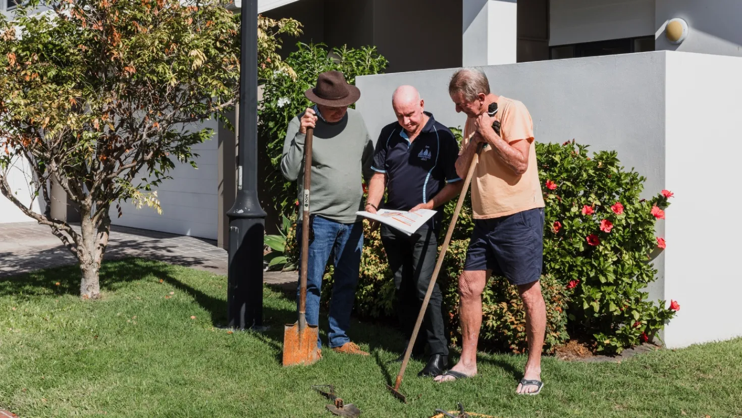 Three men with shovels and garden hoes read a guide on how hazards can affect their local area.