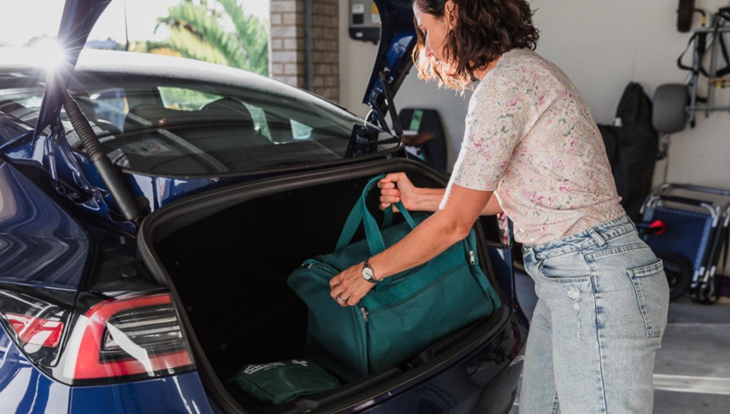 Woman loading a suitcase into a car boot as part of an emergency plan preparation.