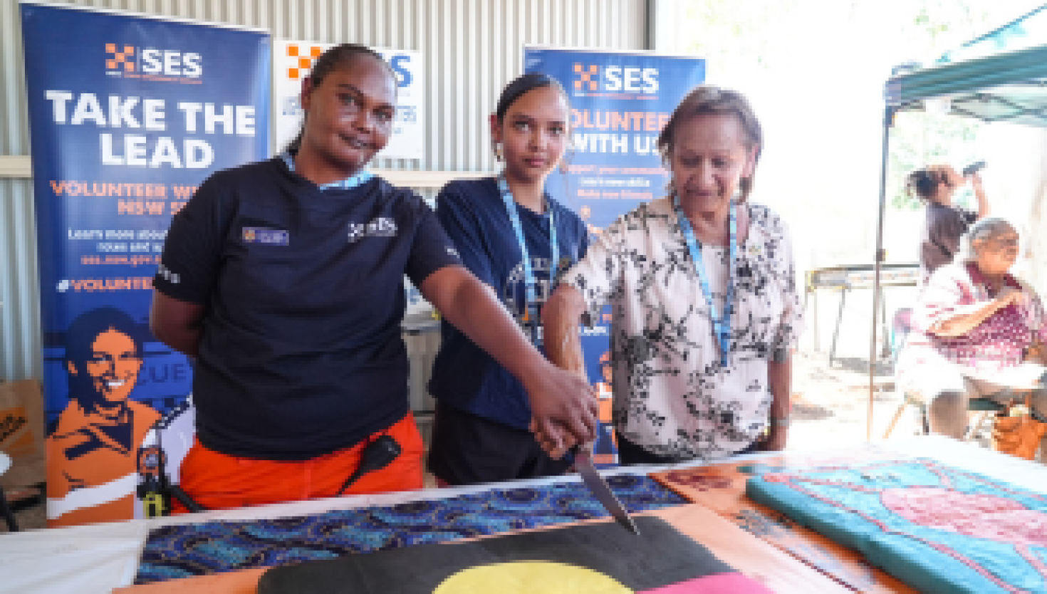 Three Lightning Ridge SES volunteers stand together, smiling as they cut into a large cake