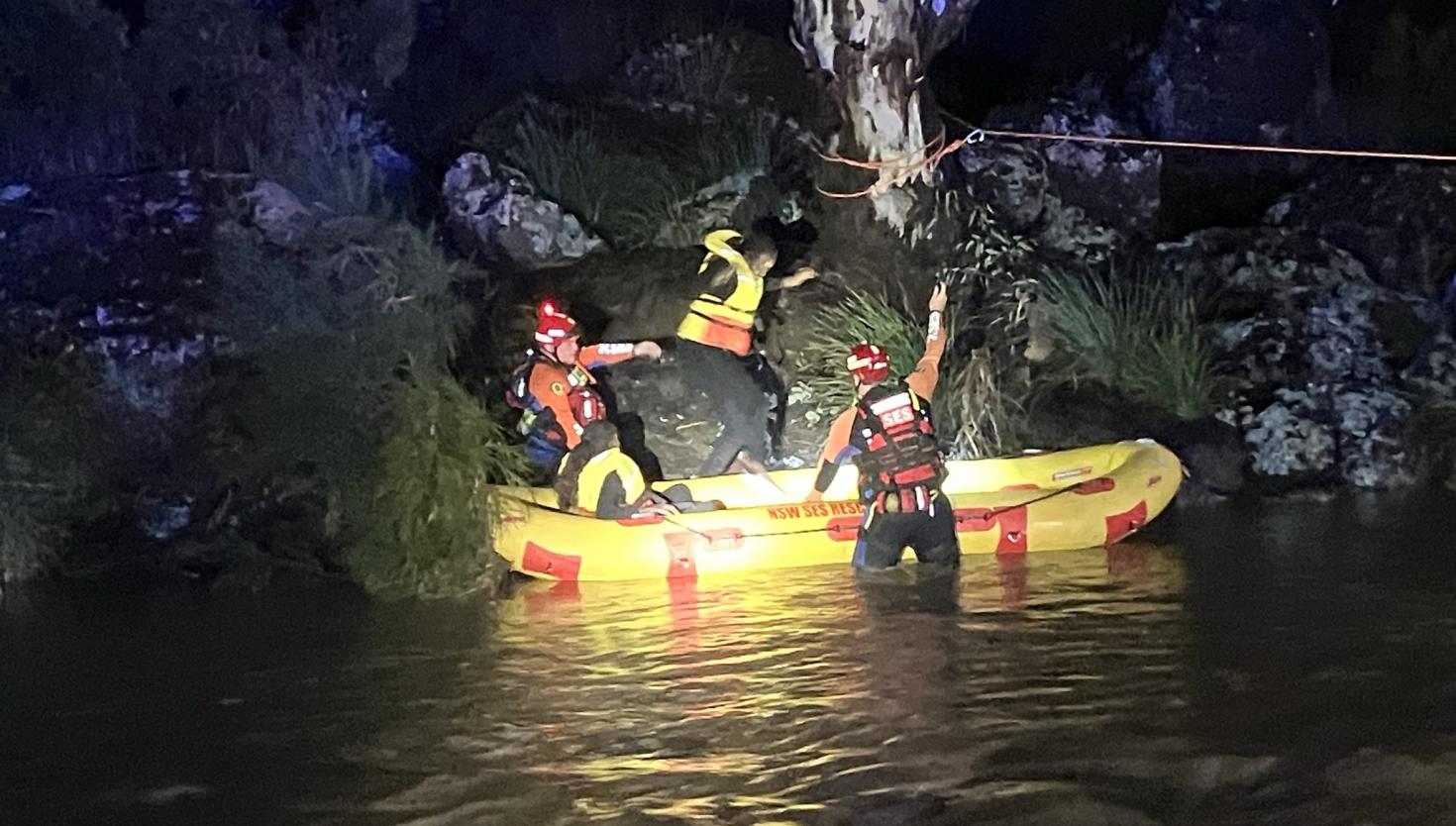A woman is rescued by two flood rescue operators in a yellow boat on the side of a river.