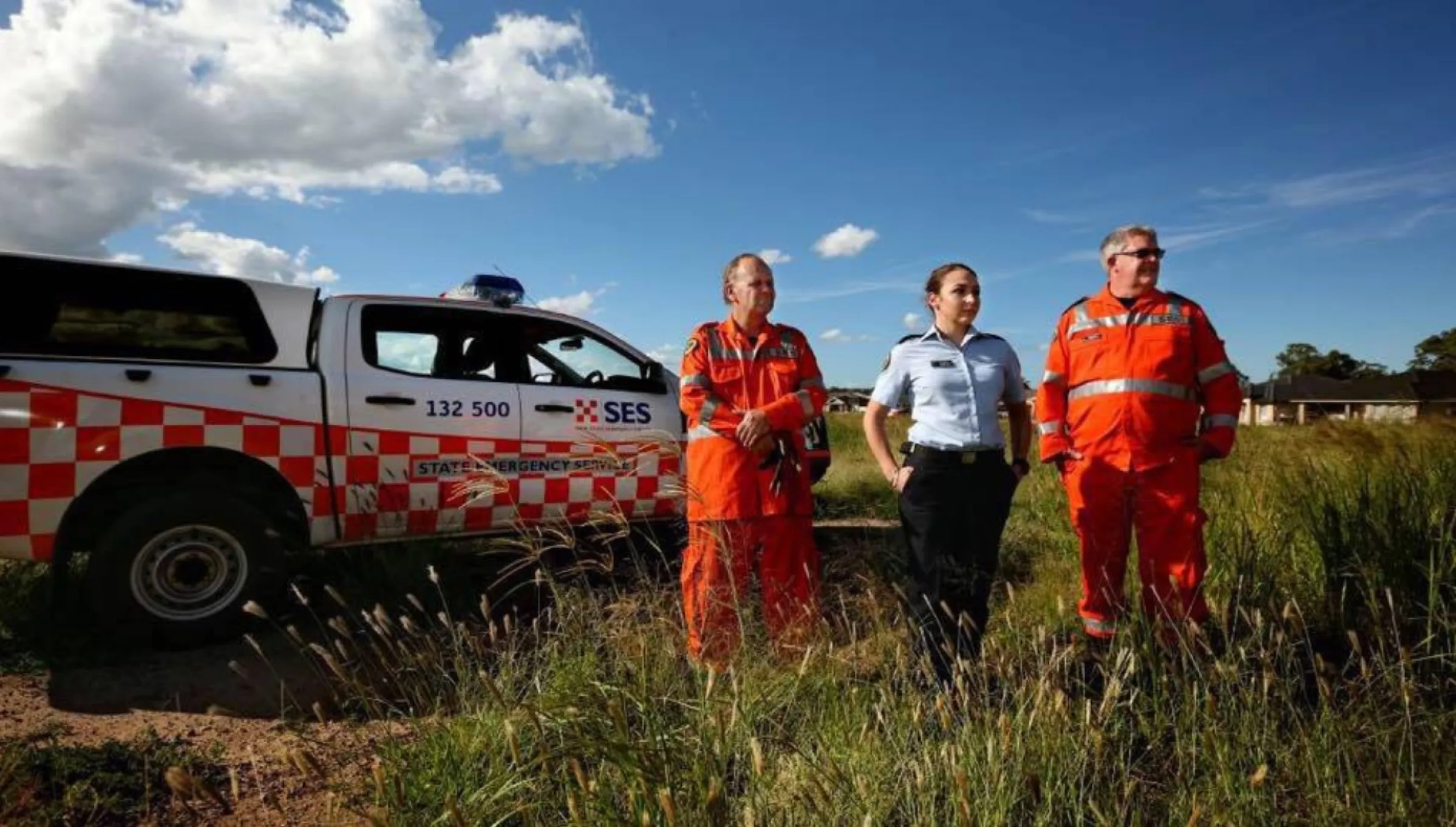 Three NSW SES members, each wearing distinct uniforms, standing in front of a NSW SES vehicle while working in the field.