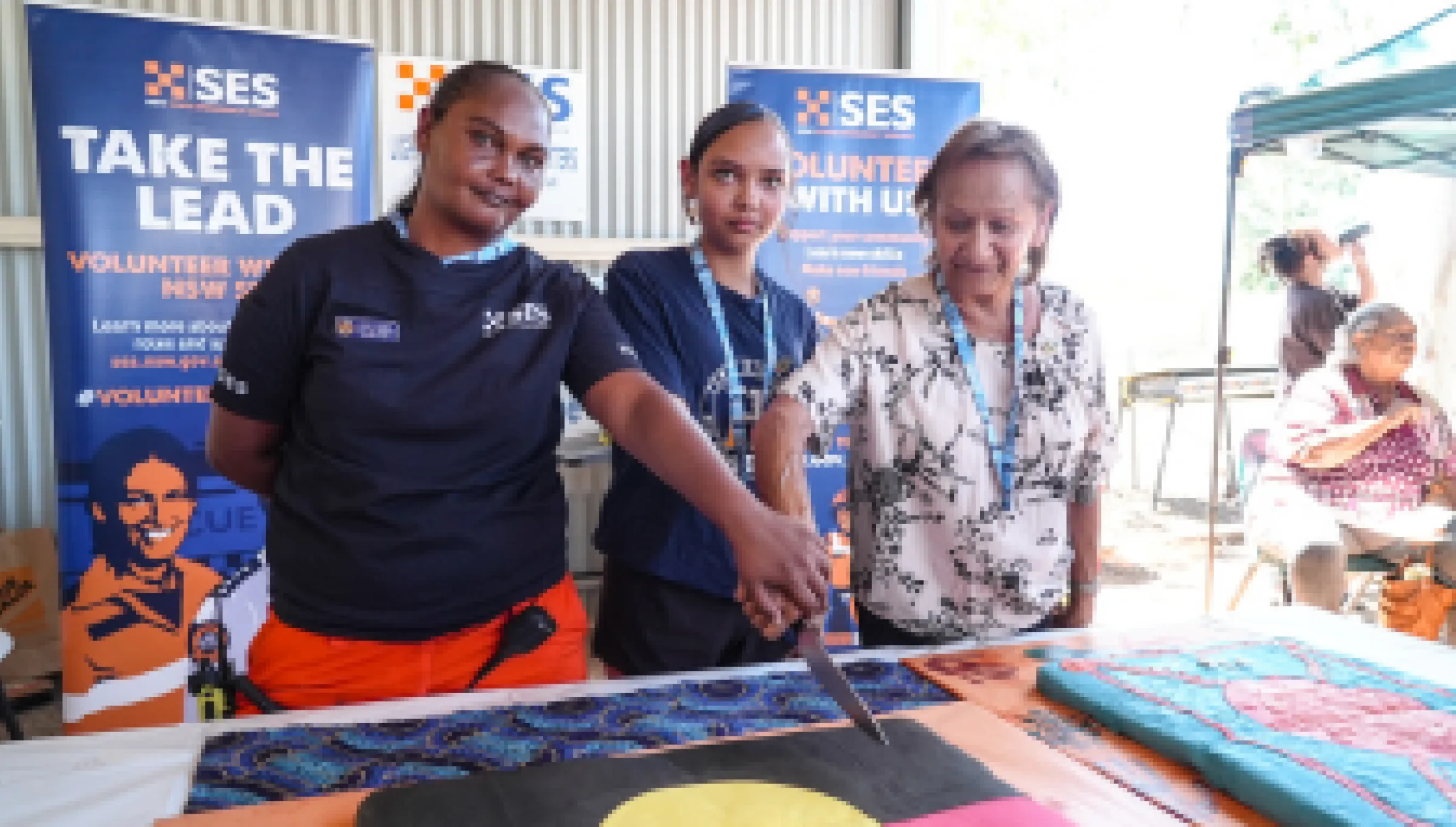 Three Lightning Ridge SES volunteers stand together, smiling as they cut into a large cake