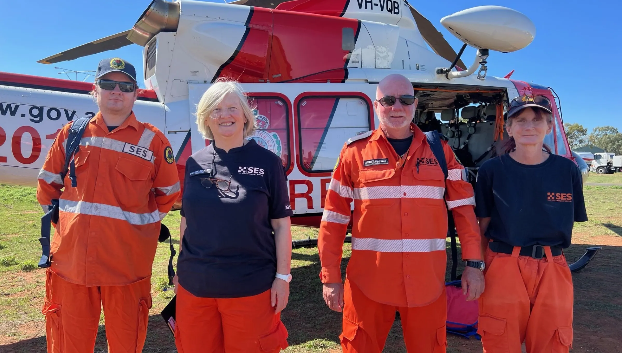 4 volunteers standing in front of a red and white helicopter