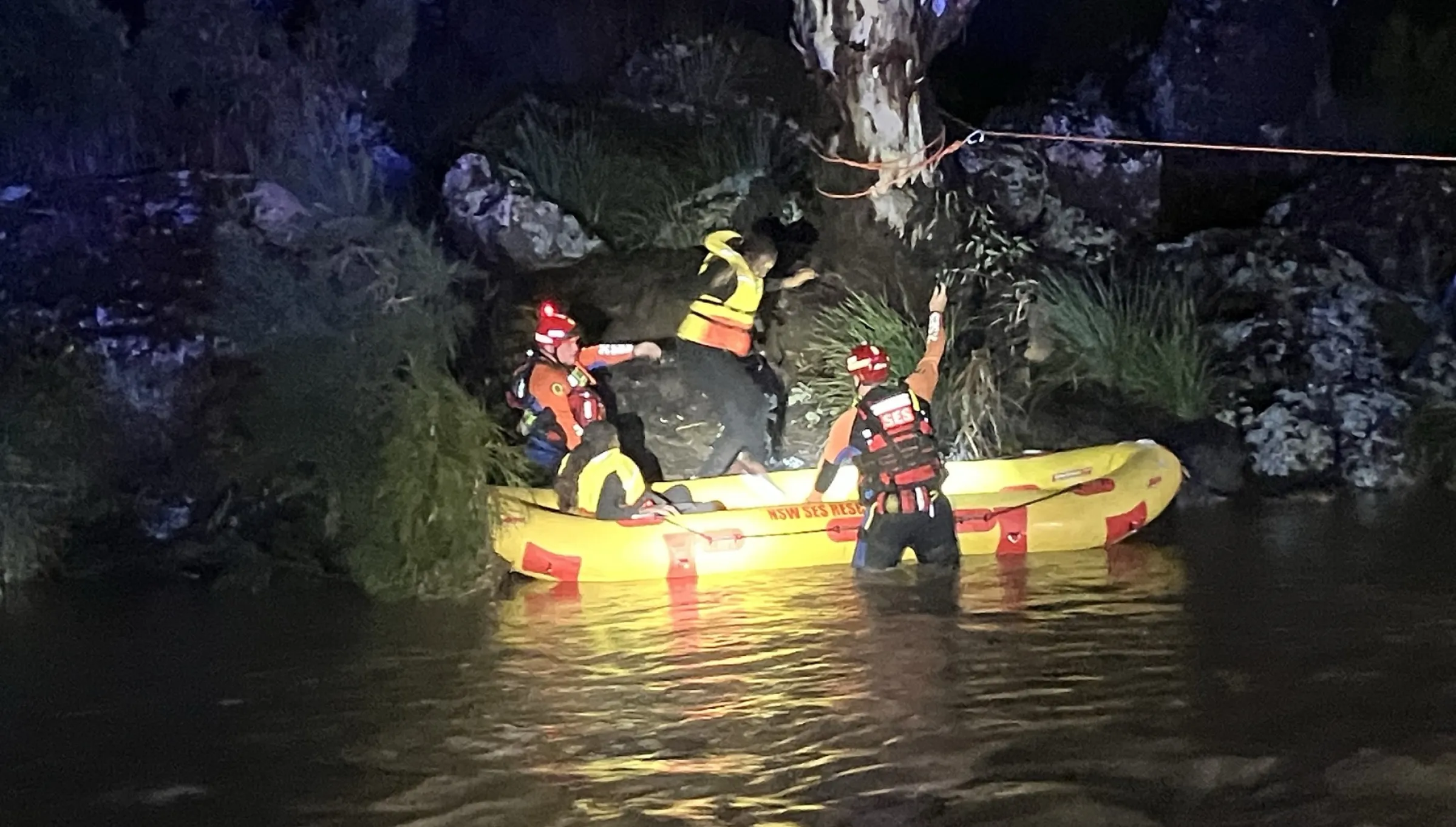 A woman is rescued by two flood rescue operators in a yellow boat on the side of a river.
