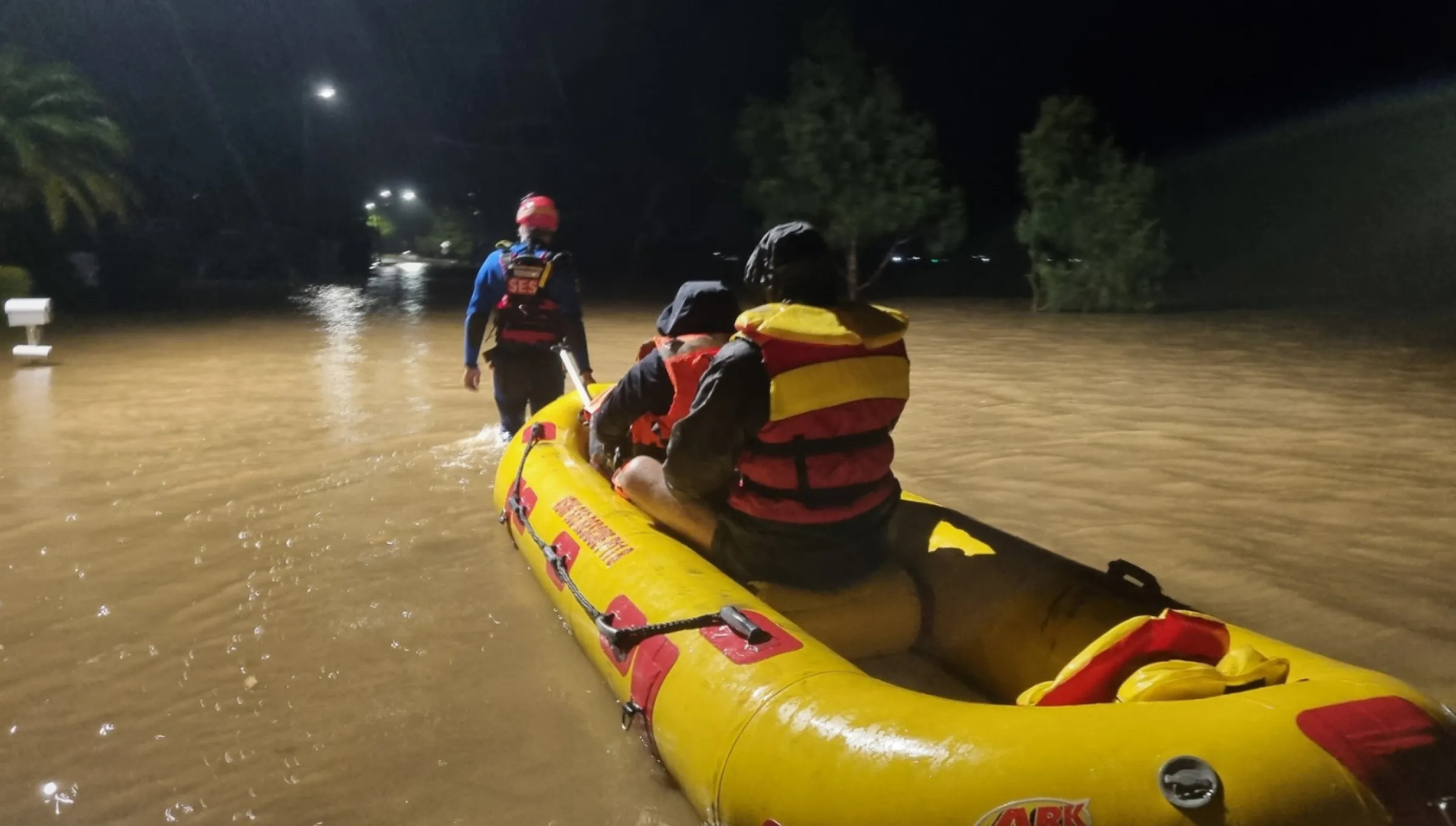 A flood rescue operate pulls a flood boat through flood water with two passengers.