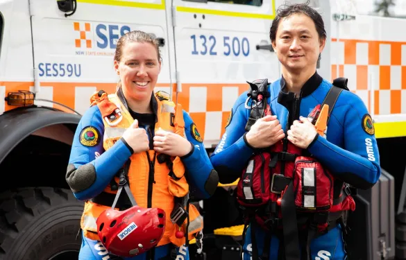 A male and female NSW SES volunteers, fully equipped in gear, standing in front of an NSW SES truck.