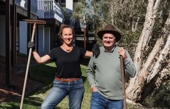 A woman and a man working together to rebuild a backyard, each holding a hoe.