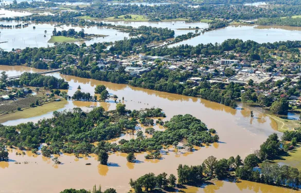 Flooded landscape in the Hawkesbury-Nepean area of NSW, with fields and trees partially submerged under murky floodwater.