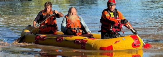 Two NSW SES volunteers rescuing a man while rowing a boat.