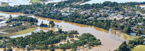 Flooded landscape in the Hawkesbury-Nepean area of NSW, with fields and trees partially submerged under murky floodwater.