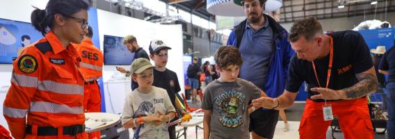 Two NSW SES volunteers, a woman and a man, engaging with a group of three children and one adult at the Easter Show event.